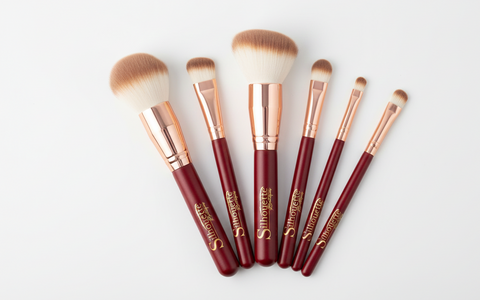 Set of makeup brushes with red handles and gold accents on a white background